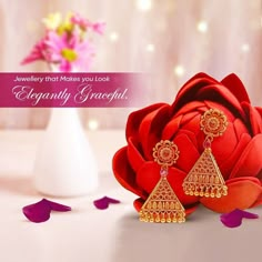 a red rose with earrings on it sitting next to a white vase filled with flowers