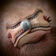 This leather wristband uses a single layer of plush natural vegetable tanned leather which is designed, carved, stamped and dyed with a Native Old West theme. A bold concho sits in the center and a smaller fluted concho serves as a snap closure. kangaroo lace details add to the Southwestern Style Brown Concho Bracelets, Rustic Brown Concho Bracelets, Rustic Brown Bracelet With Concho, Southwestern Hand-tooled Brown Bracelets, Rustic Leather Concho Bracelets, Rustic Brown Cuff Bracelet With Concho, Rustic Hand Tooled Leather Bracelets, Brown Hand Tooled Western Bracelets, Southwestern Hand Tooled Brown Cuff Bracelet