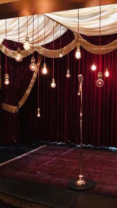 a stage with lights hanging from the ceiling and red curtains on the wall behind it