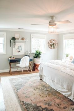 a bedroom with white bedding and rugs on the floor, windows in the background