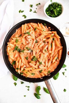 a skillet filled with pasta and sauce on top of a white table next to some parsley