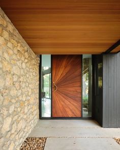 the entrance to a modern home with stone walls and wood door, surrounded by gravel