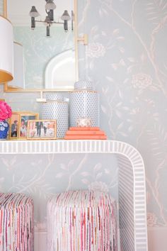 a white shelf with two stools and a mirror on the wall above it in a pink room