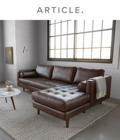 a brown leather couch sitting on top of a rug in front of a large window