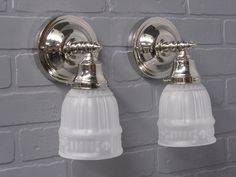 two light fixtures mounted on the side of a white brick wall next to each other