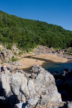 there is a large rock on the side of the water with trees in the background