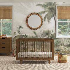 a baby's room with a palm tree wallpaper and a round mirror above the crib