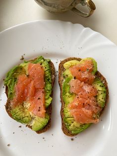 two pieces of bread with salmon and avocado on them sitting on a plate