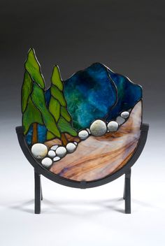 a glass sculpture with rocks and trees on it's side, in front of a gray background