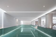 an indoor swimming pool surrounded by white walls and columns with lights on the ceiling above it