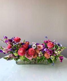 an arrangement of flowers in a vase on a white table top with grey walls behind it