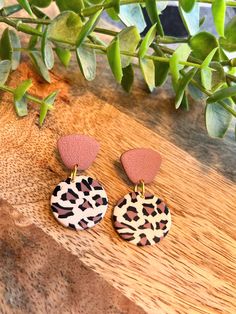 two pairs of leopard print and pink leather earrings sitting on top of a wooden table