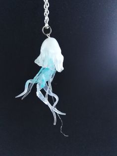 a blue and white jellyfish necklace on a black background with a chain attached to it