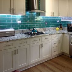 a kitchen with white cabinets and green tile backsplash in the backround