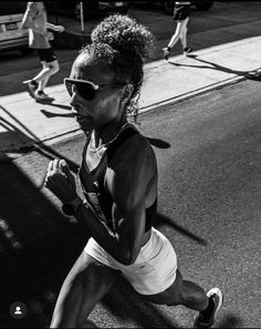 a black and white photo of a woman running down the street with other people in the background