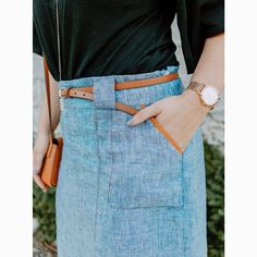 a woman wearing a blue jean skirt with her hands in her pockets and a watch on her wrist