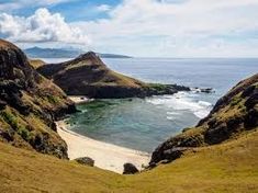 the beach is surrounded by green hills and blue water with white clouds in the sky