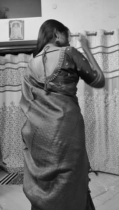 a woman standing in front of a mirror wearing a sari and looking at her hair