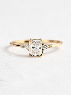 an engagement ring with a square cut diamond and three small diamonds on the band, set in yellow gold