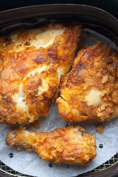 three pieces of fried chicken sitting in an air fryer with melted cheese on top