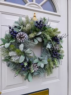 a wreath on the front door of a house decorated with greenery and pine cones