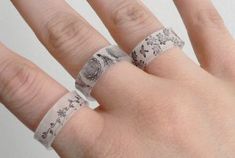 a person's hand with two wedding rings on top of their fingers and the ring has flowers all over it