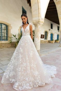 a woman standing in front of a building wearing a wedding dress with flowers on it