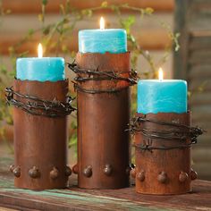 two blue candles sitting on top of a wooden table next to barbed wire and leaves