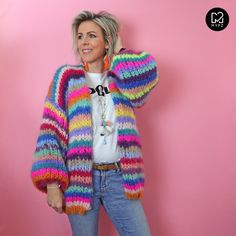 a woman standing in front of a pink wall wearing a multicolored cardigan