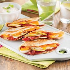 four quesadillas on a white plate with limes and water in the background