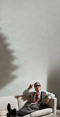 a man sitting on top of a white couch in front of a wall with the shadow of a tree