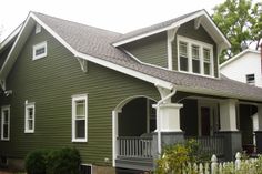 a green house with white trim on the front porch and two story windows, surrounded by greenery