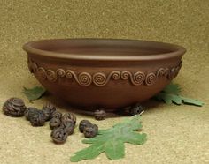 a brown bowl sitting on top of a table next to leaves and acorns