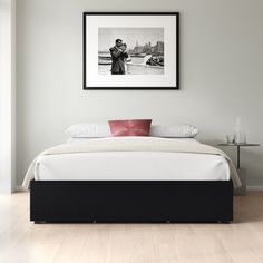 a black and white photo hangs above a bed in a room with hardwood floors, framed artwork on the wall