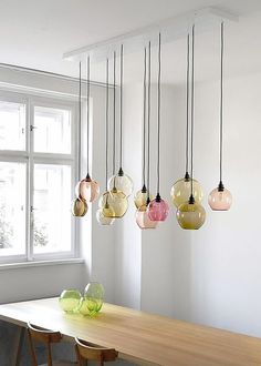 a dining room table and chairs with hanging glass lights above it, in front of a window