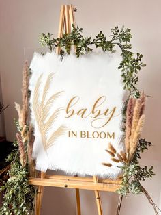 a baby in bloom sign sitting on top of a easel next to some plants