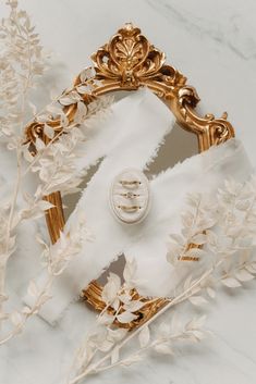 a white and gold frame sitting on top of a marble counter next to plants with leaves around it