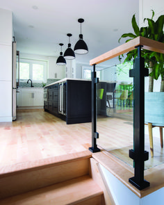 an open kitchen and dining room with wood flooring, black pendant lights hanging from the ceiling