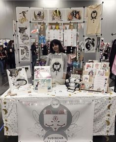 a woman standing in front of a table covered with pictures and art work on it