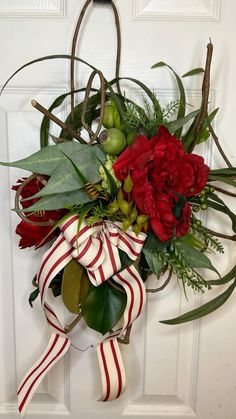 a wreath with red flowers and greenery hanging on a door