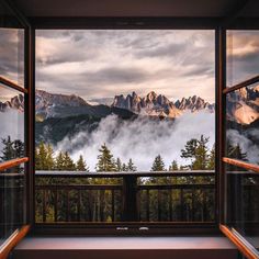 an open window looking out at the mountains and clouds in the distance with trees on either side