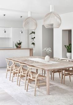 a dining room table and chairs in front of a kitchen with white walls, potted plants and hanging lights