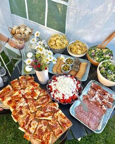 a table filled with lots of food on top of a grass covered field next to a window