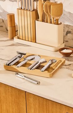 a wooden cutting board with knives and spoons on it next to other kitchen utensils