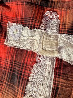 a cross made out of fabric and lace on a red plaid cloth with white crochet