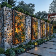 a stone wall with plants growing on it and lights shining in the windows at night