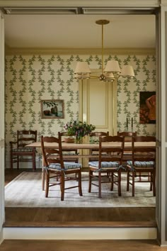 a dining room table and chairs in front of a wall papered with floral designs