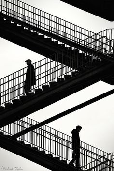 two people are walking up and down the stairs in an industrial area with metal balconies