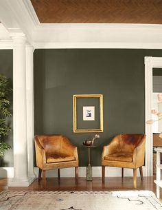 two brown chairs sitting next to each other on top of a hard wood floor in front of a green wall