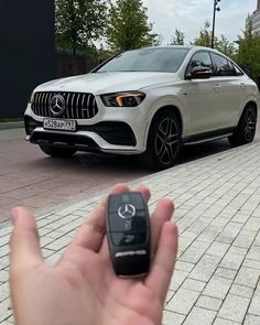 a hand holding a car key in front of a white mercedes suv parked on the street